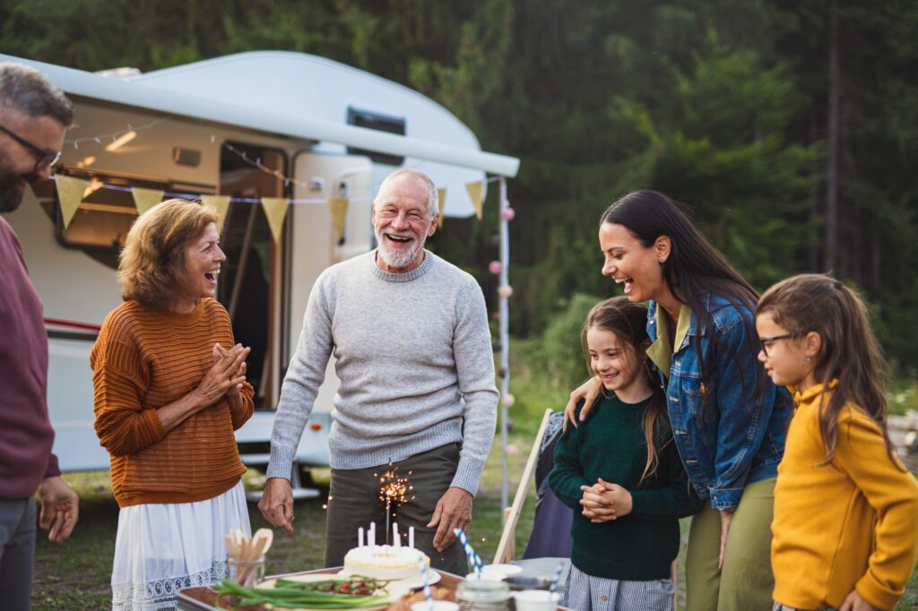 Multi-generation family celebrating birthday outdoors at campsite, caravan holiday trip